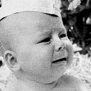 Baby wearing hat sitting outdoors on blanket.
