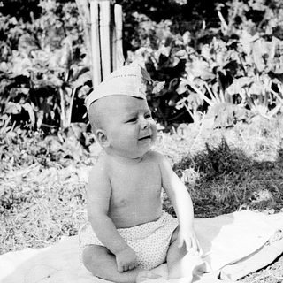 Baby wearing hat sitting outdoors on blanket.