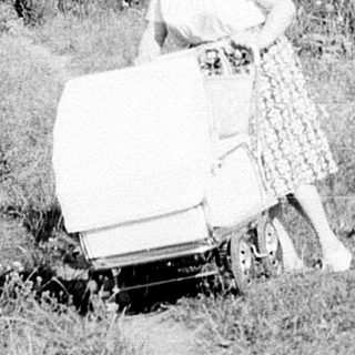 Person pushing lawn mower on grassy path.