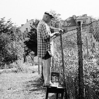 Old man repairing chain-link fence outdoors.