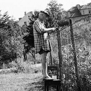 Child drinking from outdoor tap near fence.