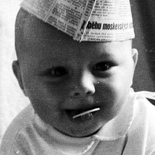 Baby wearing newspaper hat indoors.