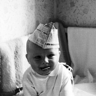 Baby wearing newspaper hat indoors.