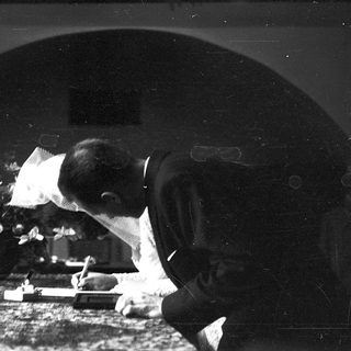 Man writing at a desk in a dimly lit room.