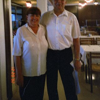 Two people posing indoors near kitchen area.