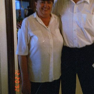 Two people posing indoors near kitchen area.