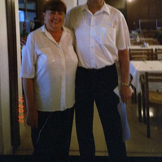 Two people posing indoors near kitchen area.