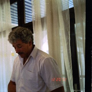 Man in light shirt looking at phone indoors.