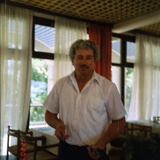 Man standing indoors near window holding remote control.