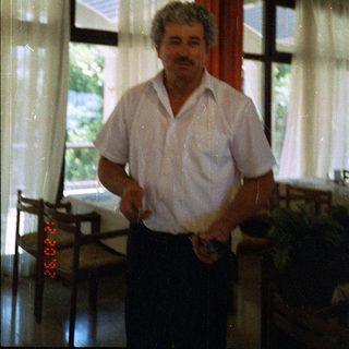 Man standing indoors near window holding remote control.