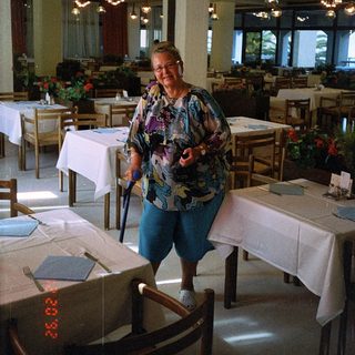 Woman smiling indoors in a restaurant with set tables.