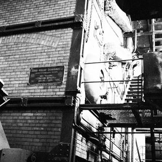 Industrial stairwell with exposed pipes and damaged wall.