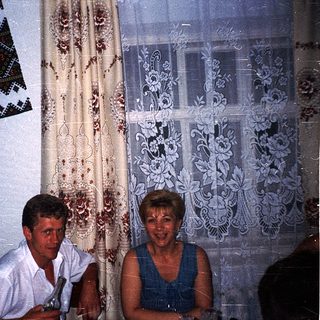 Two people seated indoors, smiling, near religious artwork.