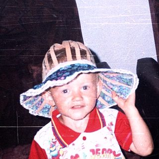 Child wearing wide-brimmed hat and colorful shirt.