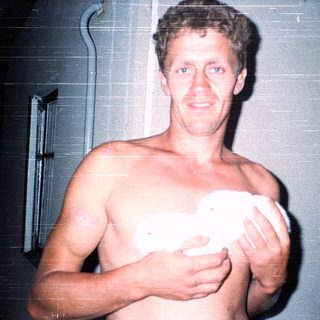 Shirtless man holding a white object indoors.