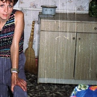 Woman standing in damp, cluttered kitchen with leaky ceiling.