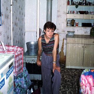 Woman standing in damp, cluttered kitchen with leaky ceiling.