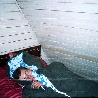 Person sleeping on bunk bed in rustic room.