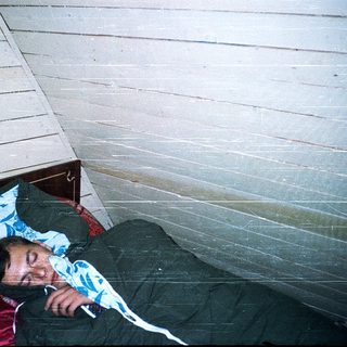 Person sleeping on bunk bed in rustic room.