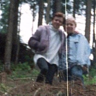 Person sitting on hillside in forested area.