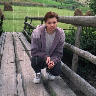 Person sitting on rustic wooden bridge in rural countryside.