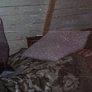 Person sitting alone indoors in rustic, dimly lit room.