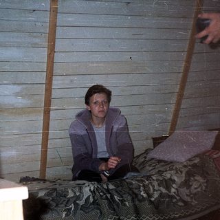 Person sitting alone indoors in rustic, dimly lit room.