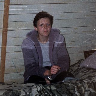Person sitting alone indoors in rustic, dimly lit room.