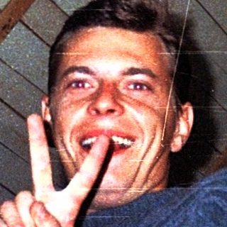 Man making peace sign indoors under slanted roof.