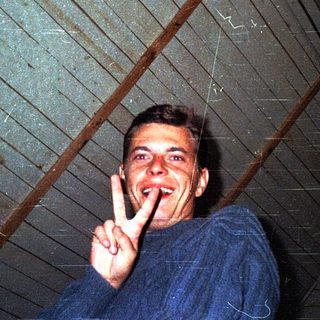 Man making peace sign indoors under slanted roof.
