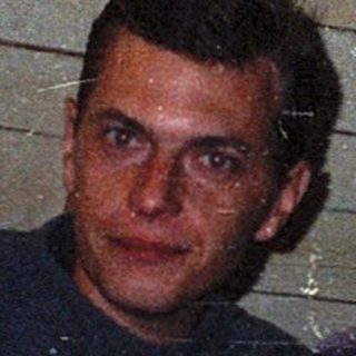 Two men sitting indoors near a wooden wall.