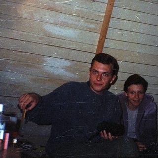 Two men sitting indoors near a wooden wall.