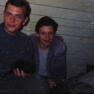 Two men sitting indoors near a wooden wall.