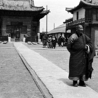 Monk in traditional robe walking in historic Asian street scene.