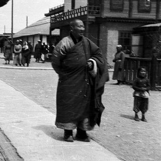 Monk in traditional robe walking in historic Asian street scene.