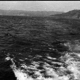 Black and white photo of rough sea waves with distant shoreline.