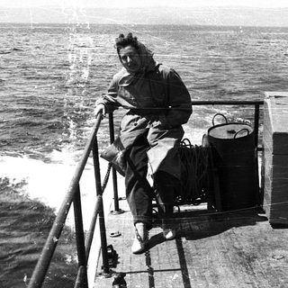 Woman sitting on ship rail, holding bag, at sea.