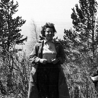 Two people in rural outdoor setting, one standing, one bending.