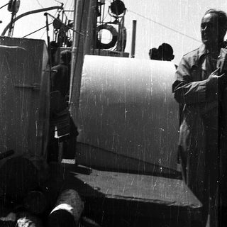 Man standing near vintage naval ship equipment.