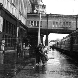 Vintage train station platform with wet pavement and pedestrians.