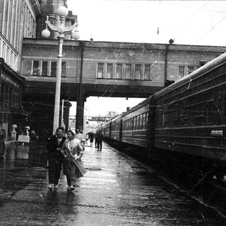 Vintage train station platform with wet pavement and pedestrians.