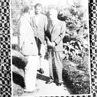 Three men outdoors holding hands with dog.