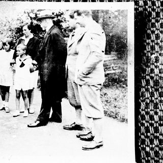 Group of people, including children, gathered outdoors in vintage clothing.
