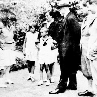 Group of people, including children, gathered outdoors in vintage clothing.