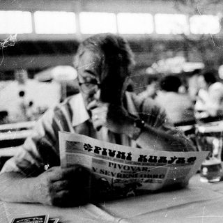 Person reading newspaper in crowded indoor seating area.