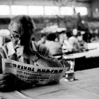 Person reading newspaper in crowded indoor seating area.