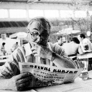 Man reading newspaper at an outdoor café.