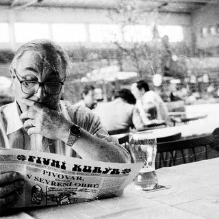 Man reading newspaper at an outdoor café.