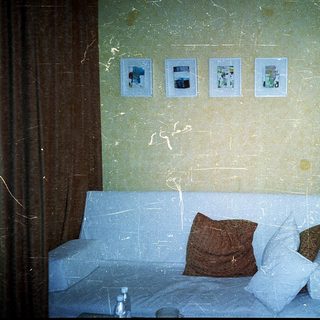 Small hotel room with sofa bed, framed photos, and worn walls.