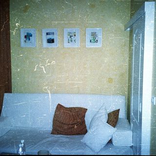 Small hotel room with sofa bed, framed photos, and worn walls.